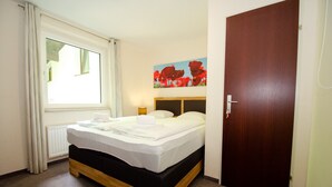 A neatly made bed with white linens, a wooden headboard, a painting of red flowers on the wall, and a closed door. - Apartment THE GOOD VIEW II - Lake & Mountain view (Zell am See)