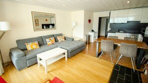 A modern living room with a grey sofa, white coffee table, and a dining area with a wooden table and grey chairs. - Apartment THE GOOD VIEW II - Lake & Mountain view (Zell am See)