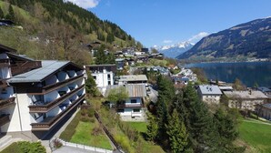 A hillside residential area with modern and traditional buildings, a parking lot, and a lake with mountains in the background. - Apartment THE GOOD VIEW II - Lake & Mountain view (Zell am See)