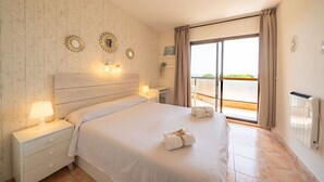 Un dormitorio con una cama grande, lámparas de noche, una mesita de noche, una ventana con cortinas y vistas al exterior.