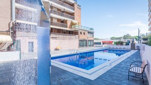 Una piscina con fuente acuática, rodeada por un balcón y la fachada de un edificio.