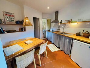 Une cuisine compacte avec un coin repas, comprenant une table en bois, des chaises, un luminaire suspendu et un four encastré.