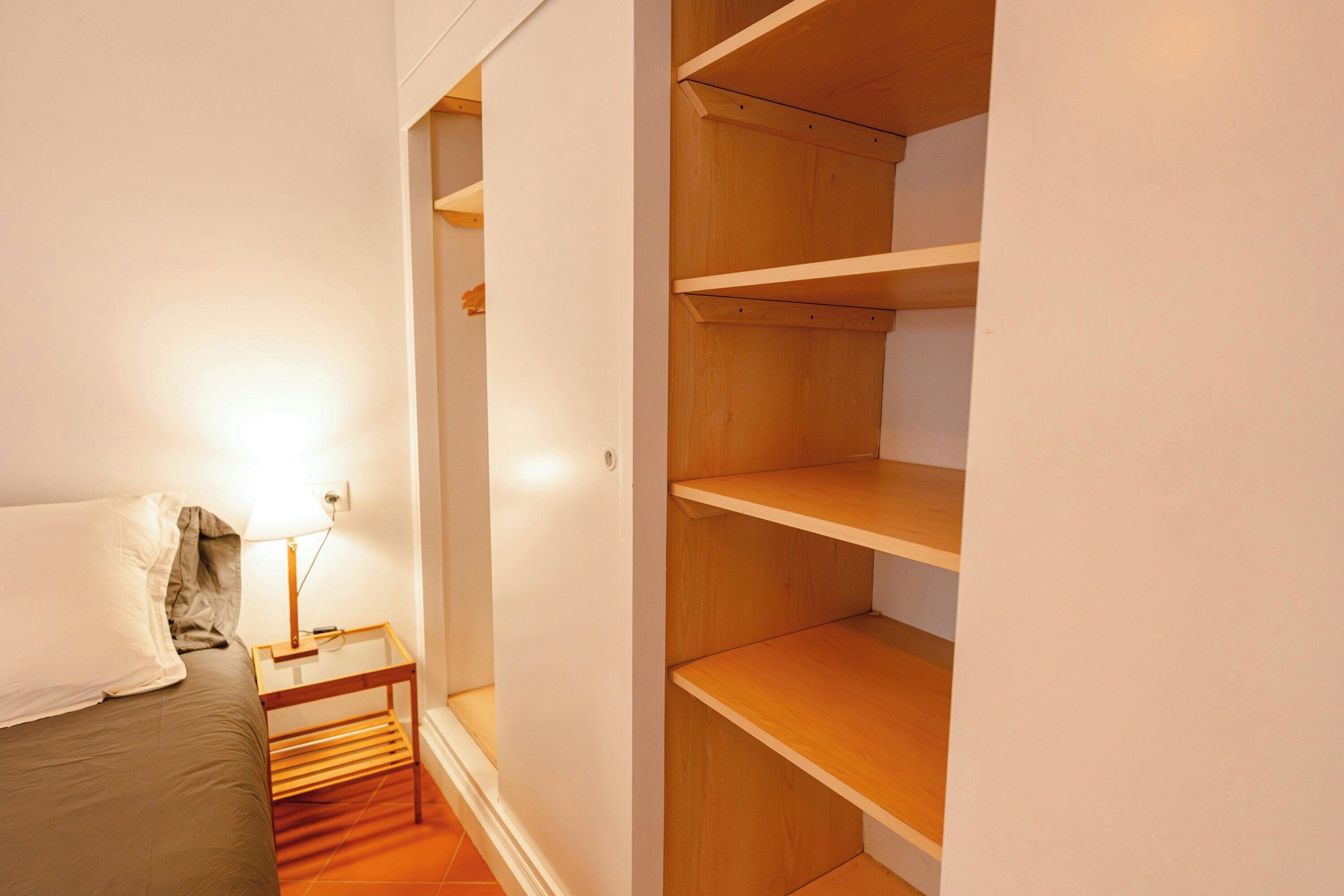 Un dormitorio con cama, mesita de noche, lámpara y un armario de madera con varios estantes.