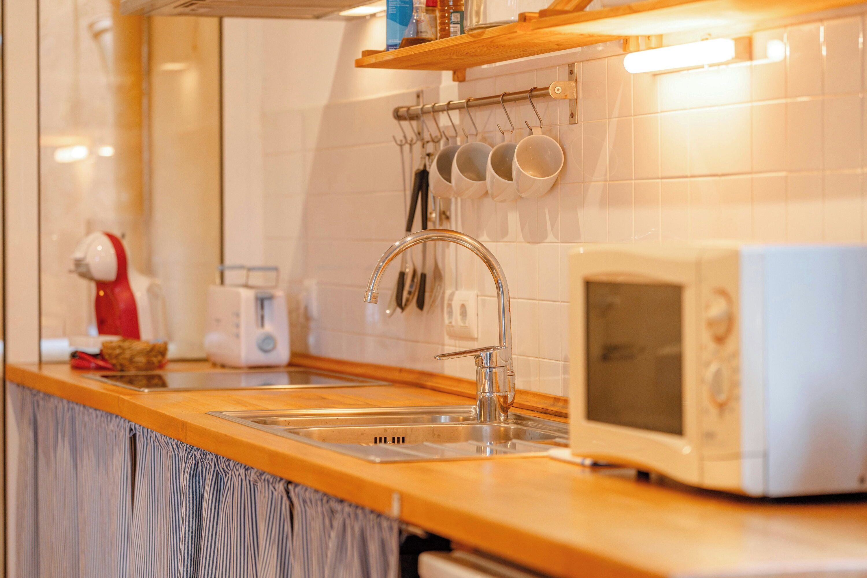 Une cuisine dotée d’un plan de travail en bois, d’un évier, d’un four à micro-ondes et d’ustensiles de cuisine suspendus.