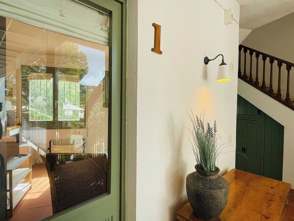A room with a large window, a wooden table, a potted plant, a wall-mounted light fixture, and a staircase.