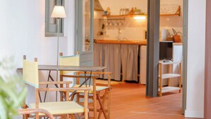 Een eethoek met een tafel en stoelen, een lamp en uitzicht op een keuken met een aanrecht en planken.