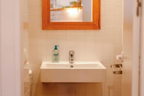 A bathroom with a white sink, a mirror with a wooden frame, and a bottle of hand soap.