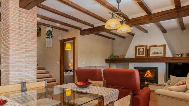 A cozy living room with a fireplace, red chairs, a glass dining table, and a staircase leading to an upper level. - Casa Rural El Abuelo Luis for 8 people (Molinicos)