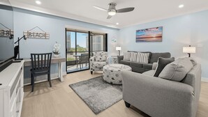 En moderne stue med en grå sofa, et rundt sofabord og et spiseområde med en stol og et bord.