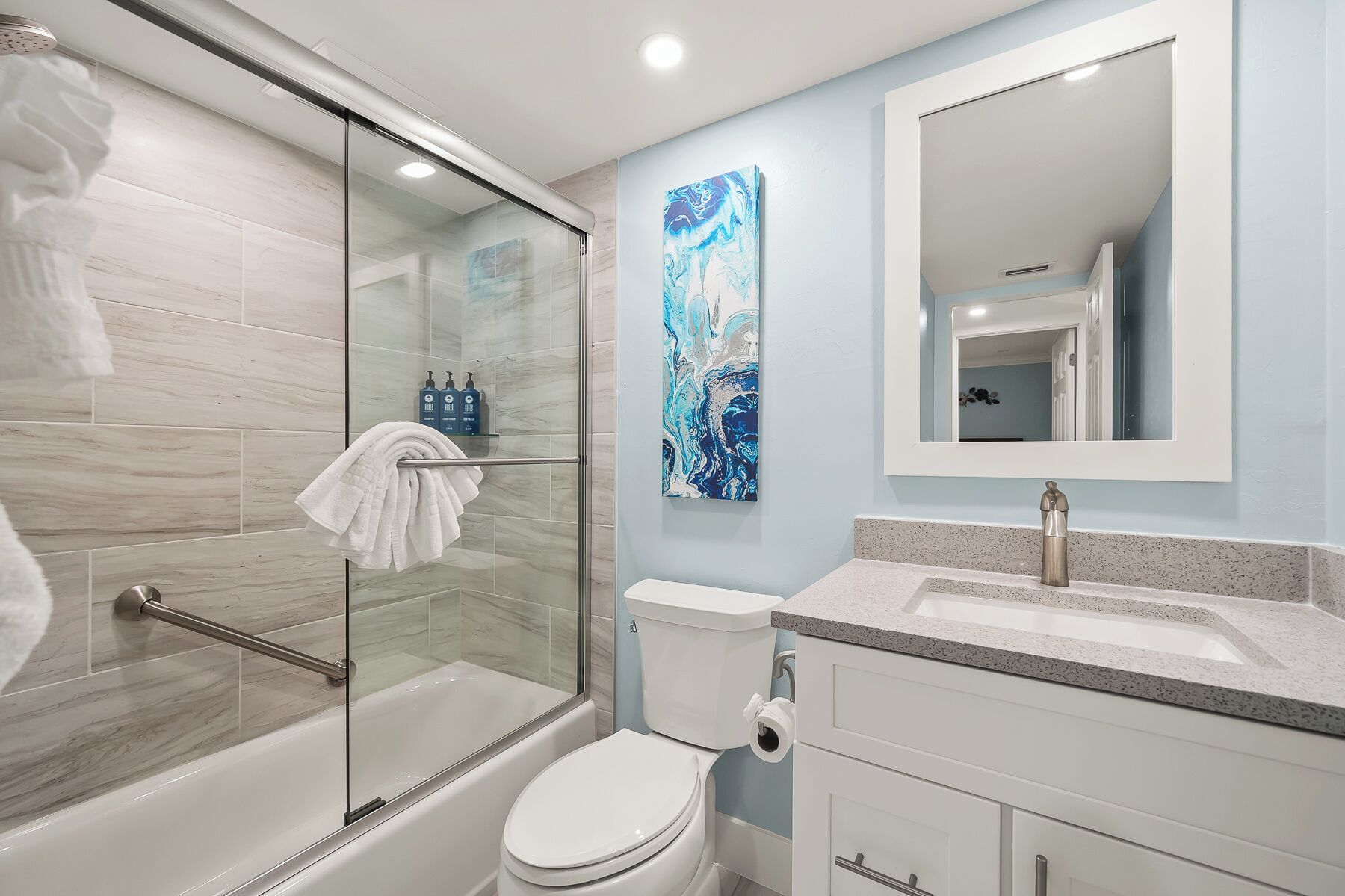 Un baño moderno con ducha envuelta en vidrio, inodoro blanco y lavamanos con encimera de granito.