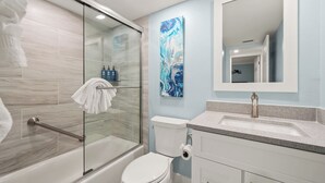 Et moderne badeværelse med en glasafskærmet brusekabine, et hvidt toilet og en vask med en bordplade i granit.
