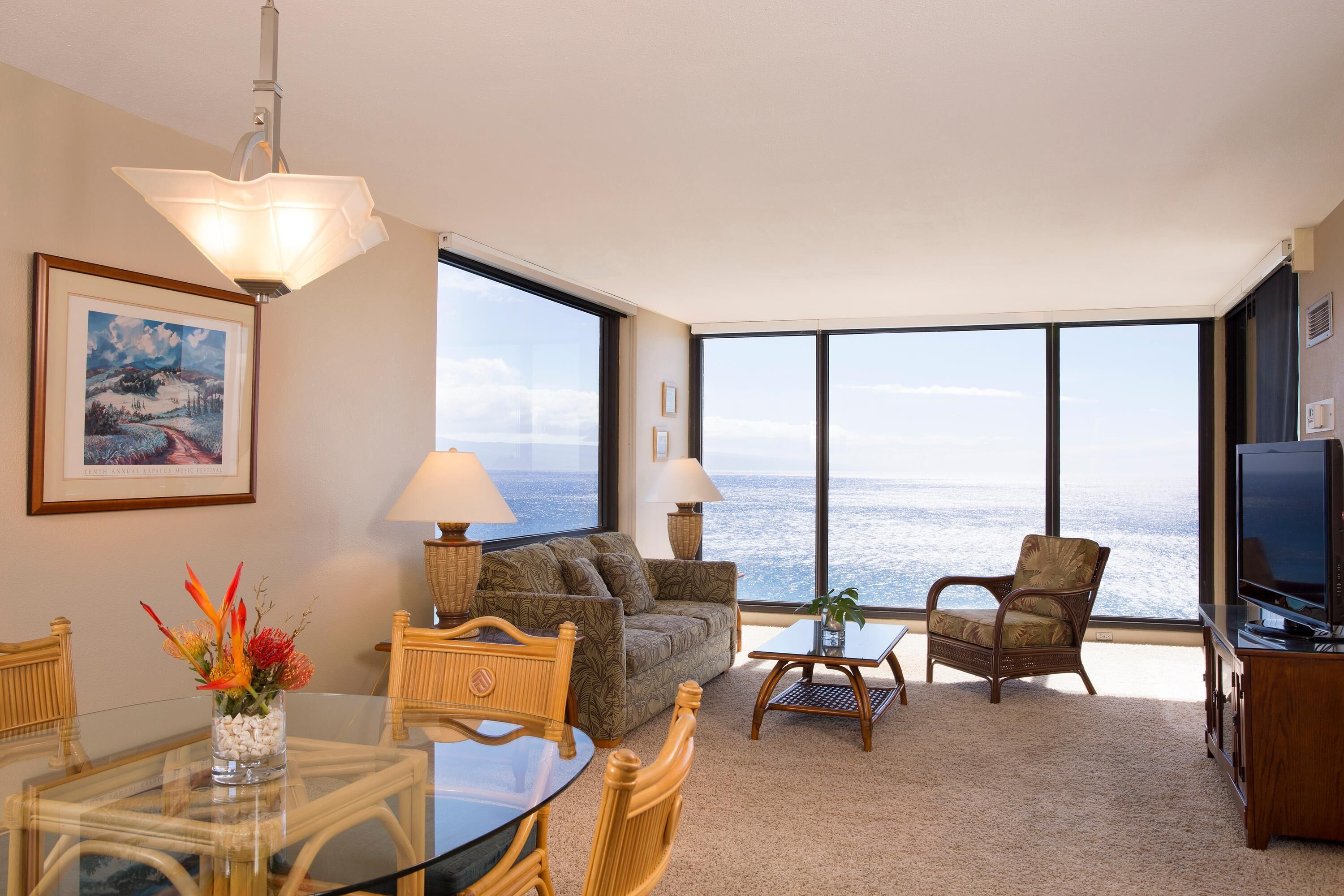 A room with a large window, a dining table, two sofas, a TV, and a painting on the wall.