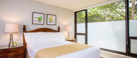 A hotel room with a large bed, two bedside tables with lamps, a window with a view of trees, and two framed pictures on the wall.
