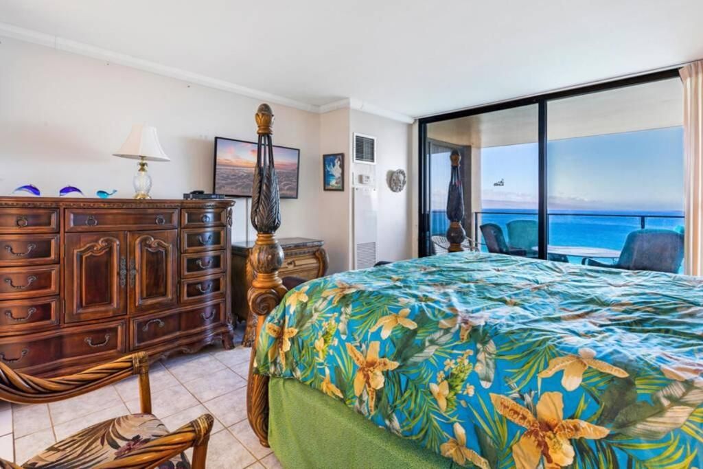 A hotel room with a bed, a wooden dresser, a chair, and a view of the ocean.