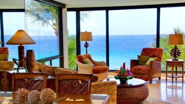 Un salón amplio con un gran ventanal con vistas al océano, amueblado con un sofá, sillones y una mesa de centro.