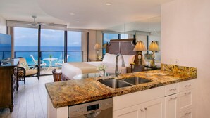 Habitación de hotel moderna con balcón, zona de cocina y un amplio ventanal con vista al océano.
