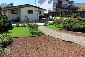 Um imóvel residencial com gramado bem cuidado, um caminho de cascalho e um pequeno jardim com arbustos e uma árvore.