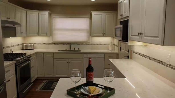 A kitchen with light-colored cabinets, a stove, and a dining area with a tray of food and two glasses.