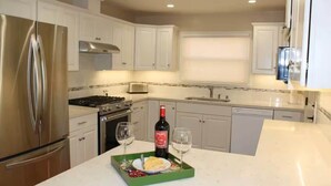 A modern kitchen with white cabinets, stainless steel appliances, and a green tray with a bottle of wine and glasses.