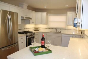 A modern kitchen with white cabinets, stainless steel appliances, and a green tray with a bottle of wine and glasses. - Manyas House  30 night minimum (Monterey)