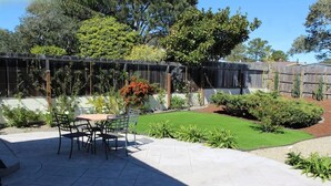 A patio area with a table and chairs, surrounded by a well-maintained lawn and various plants.