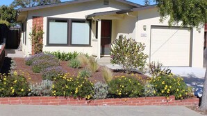 A single-story house with a garage, a front porch, and a landscaped garden with various plants and flowers.