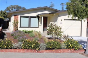 A single-story house with a garage, a front porch, and a landscaped garden with various plants and flowers.