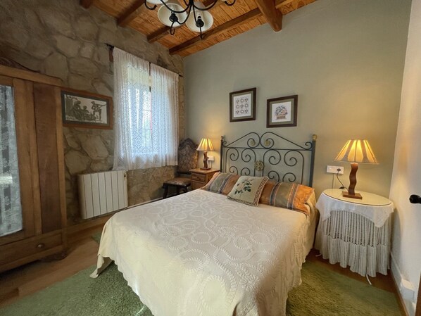 Un dormitorio con pared de piedra, una cama con colcha estampada, dos lámparas de noche y cuadros enmarcados en la pared.