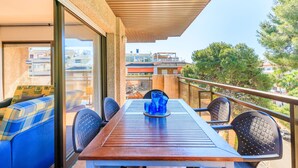 A balcony with a wooden table, blue upholstered chairs, and a glass vase. - Centrally-Located Apartment · AirCon · Shared Pool · UHC CASALMAR 223 (Salou)