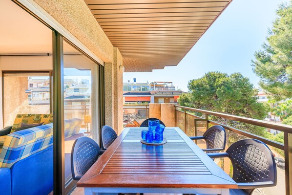 A balcony with a wooden table, blue upholstered chairs, and a glass vase.