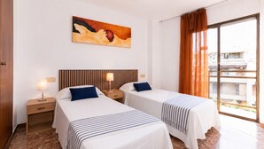A hotel room with two beds, a ceiling fan, a painting on the wall, and a view through a large window. - Centrally-Located Apartment · AirCon · Shared Pool · UHC CASALMAR 223 (Salou)