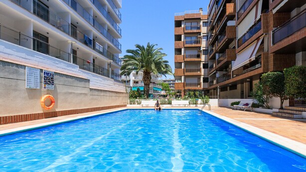 A swimming pool with a palm tree and a building with balconies in the background. - Centrally-Located Apartment · AirCon · Shared Pool · UHC CASALMAR 223 (Salou)