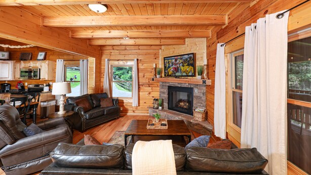 A log cabin interior with a fireplace, leather furniture, and a kitchen area. - Private Fire Pit, Wheelchair Accessible, Hot Tub, Pool Table (Sevierville)