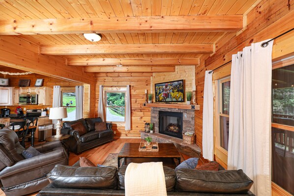 A log cabin interior with a fireplace, leather furniture, and a kitchen area. - Private Fire Pit, Wheelchair Accessible, Hot Tub, Pool Table (Sevierville)