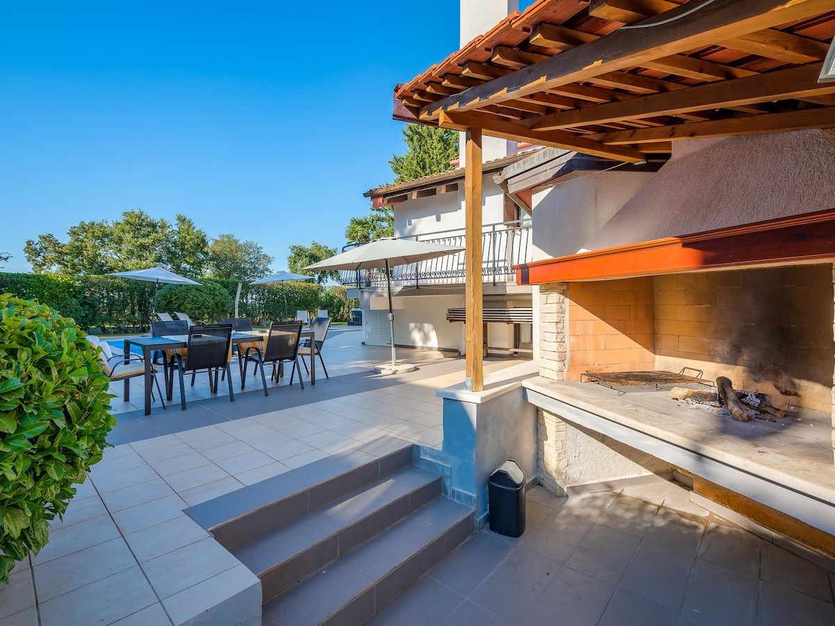 An outdoor patio with a barbecue grill, a covered seating area, and a pool.