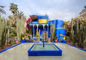 A building with a blue facade and a central fountain, surrounded by cacti and palm trees.