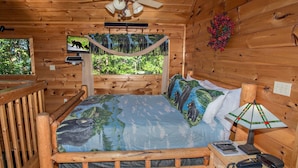 Un dormitorio de cabaña de madera con una cama, un escritorio, una lámpara y un televisor.