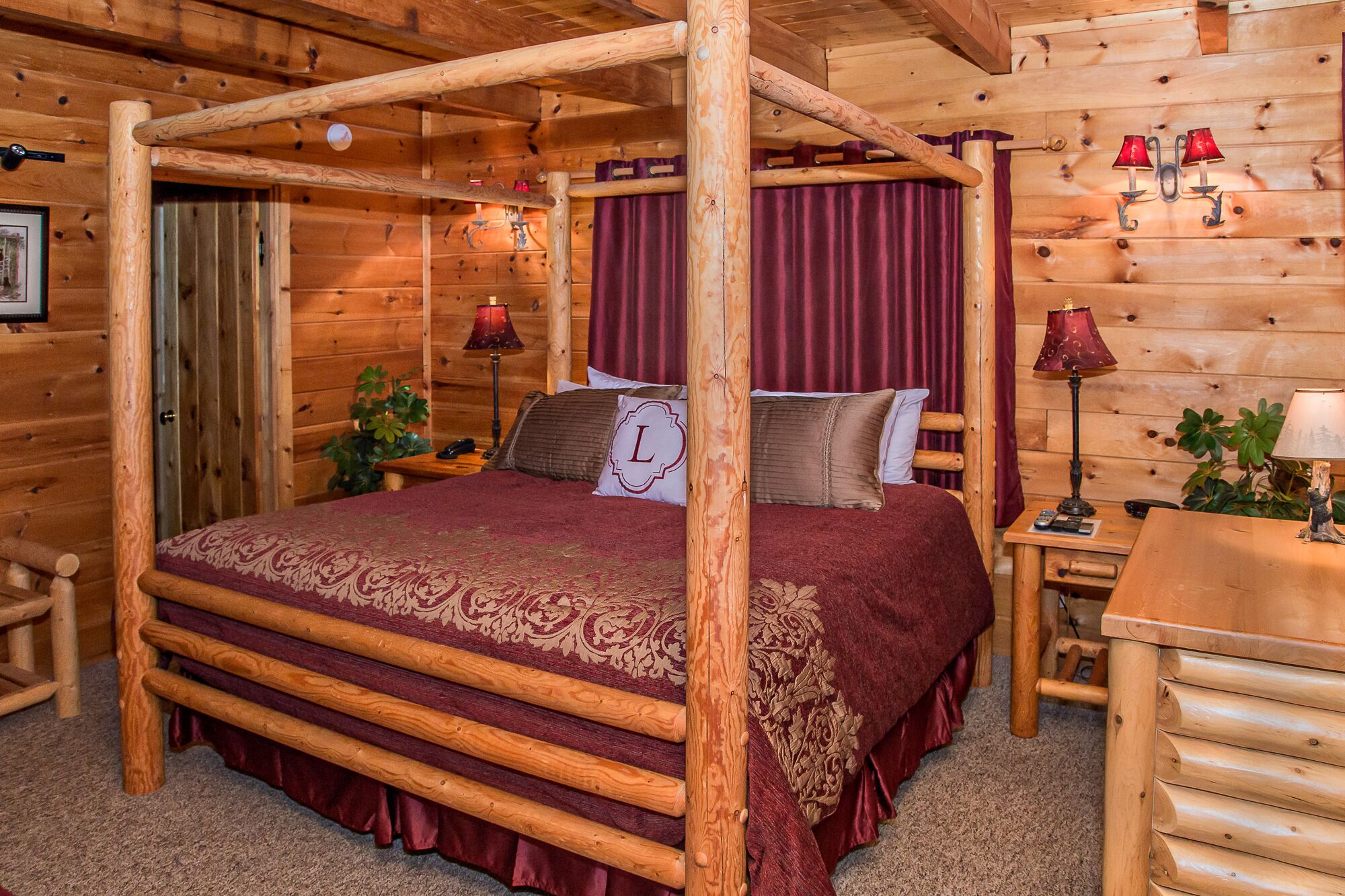 Un dormitorio tipo cabaña de madera con cama con dosel, cortinas rojas y dos lámparas de noche.