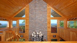 Una cabaña de madera con chimenea de piedra, barandillas de madera y ventanas amplias que ofrecen vistas panorámicas.