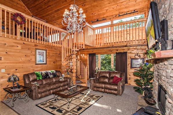 A spacious wooden cabin with a loft bedroom, a fireplace, and a chandelier.