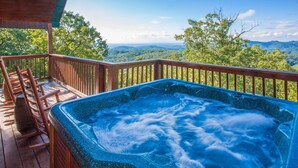 Un jacuzzi en una terraza de madera con una vista panorámica de montañas y árboles.
