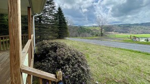 A wooden deck with a view of a rural landscape, including a road and distant hills.