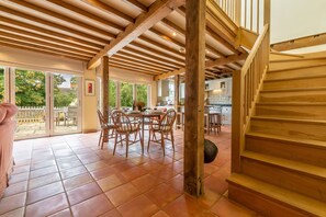 Un grand espace à manger avec une table et des chaises en bois, une cuisine à l’arrière-plan et un escalier en bois.