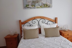 Un lit bien fait, recouvert d’une couette blanche, avec deux oreillers beige et une tête de lit en bois ornée d’un motif en métal noir.