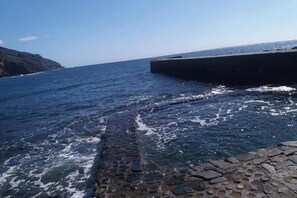 A coastal scene with a rocky shoreline, a breakwater, and calm sea.