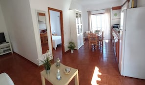 A spacious living area with a dining table, kitchen, and a bedroom visible through an open door.
