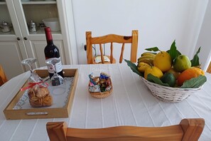 Een eettafel met een mand fruit, een fles wijn en een dienblad met een ingepakt voorwerp.