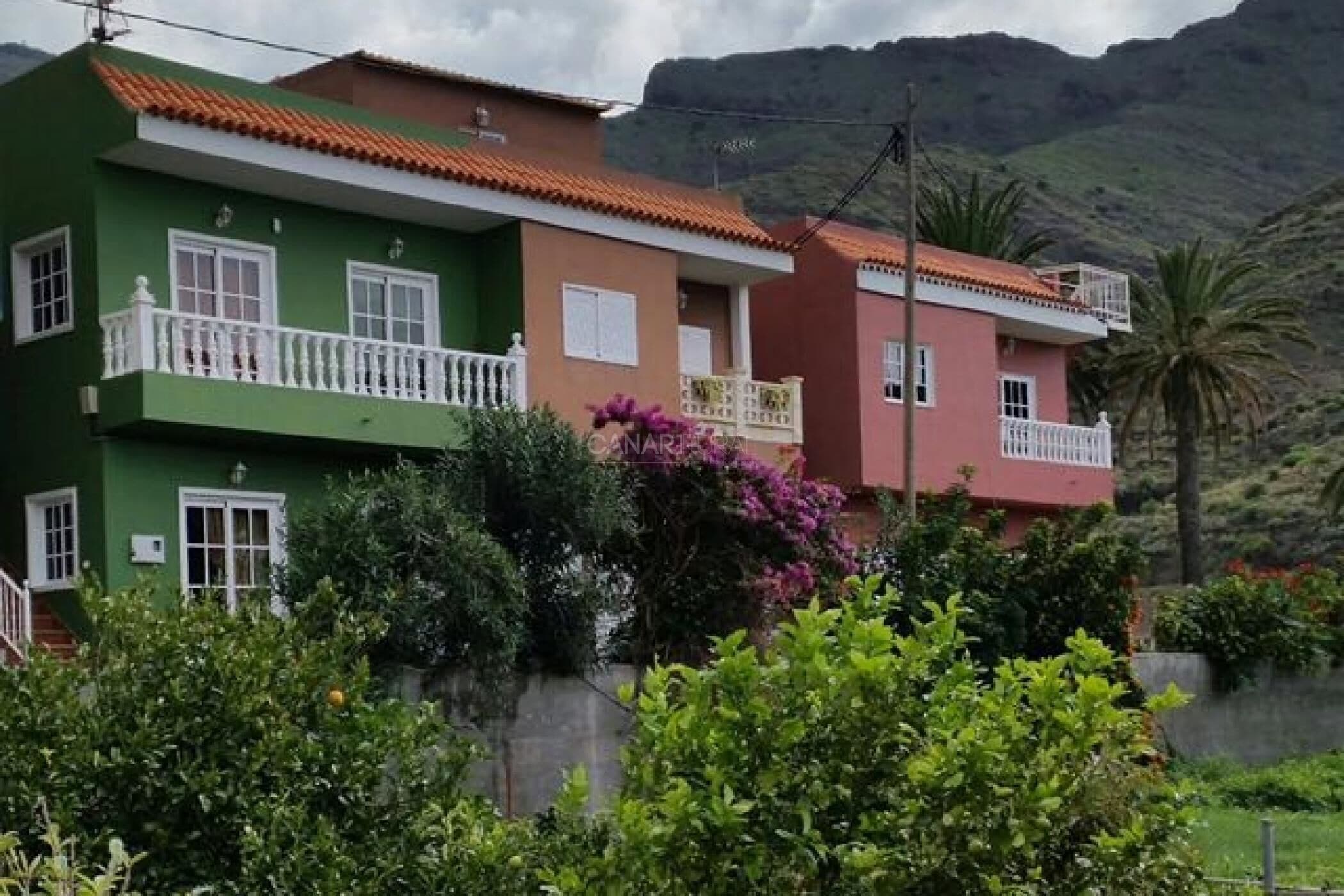 A residential building with a red-tiled roof, balconies, and lush greenery.