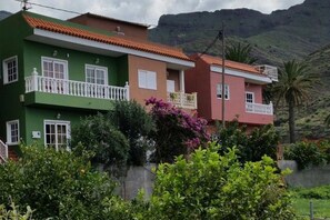 Un edificio residencial con techo de tejas rojas, balcones y abundante vegetación.