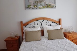 Een net opgemaakt bed met een witte deken, twee beige kussens en een houten hoofdbord met een zwart metalen design.